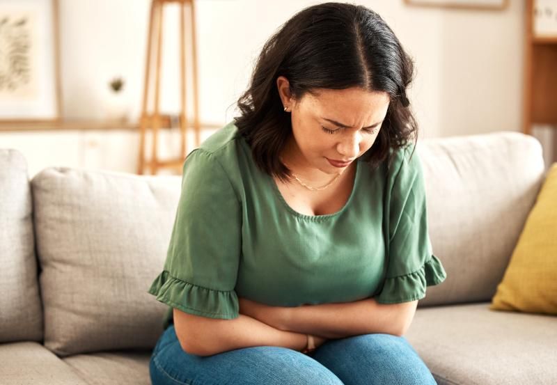 Frau mit Bauchschmerzen sitzt auf einer Couch