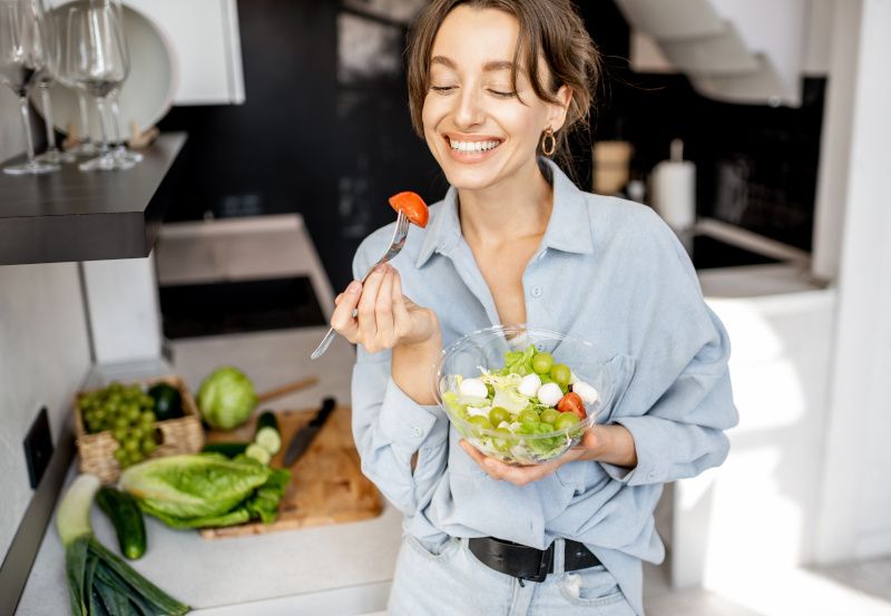 Fröhliche Frau isst Salat in der Küche