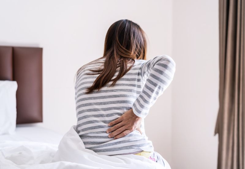 Frau mit Rückenschmerzen sitzt in ihrem Bett