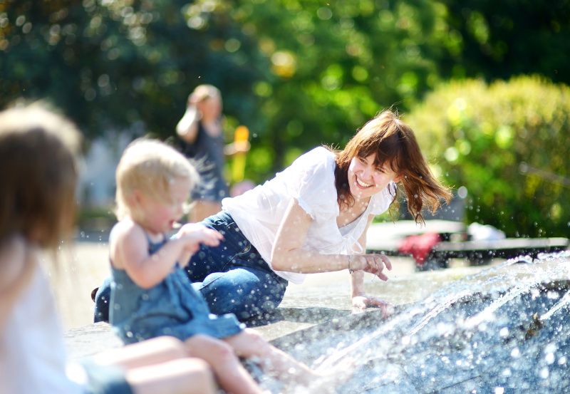 Junge Frau und zwei Kinder kühlen sich in der Stadt bei einem Brunnen ab