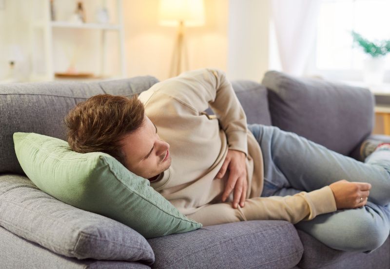 Mann liegt auf der Couch und hat Bauchschmerzen