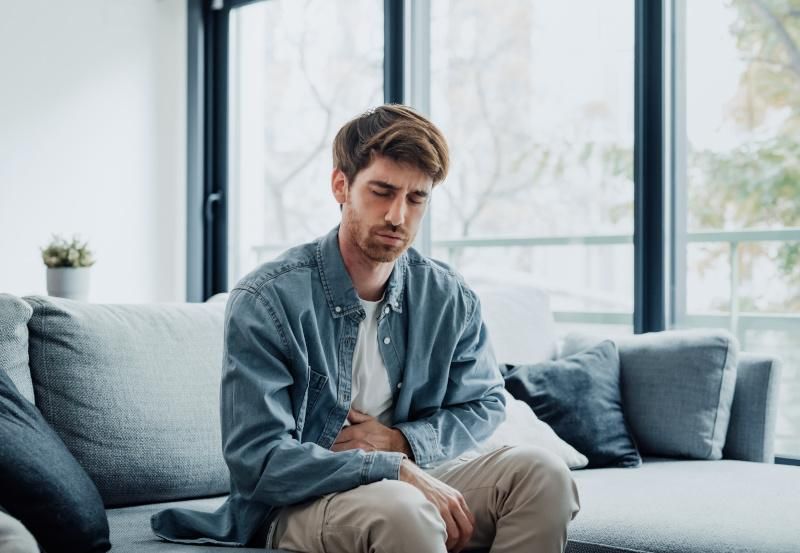 Mann mit Bauchschmerzen sitzt auf der Couch