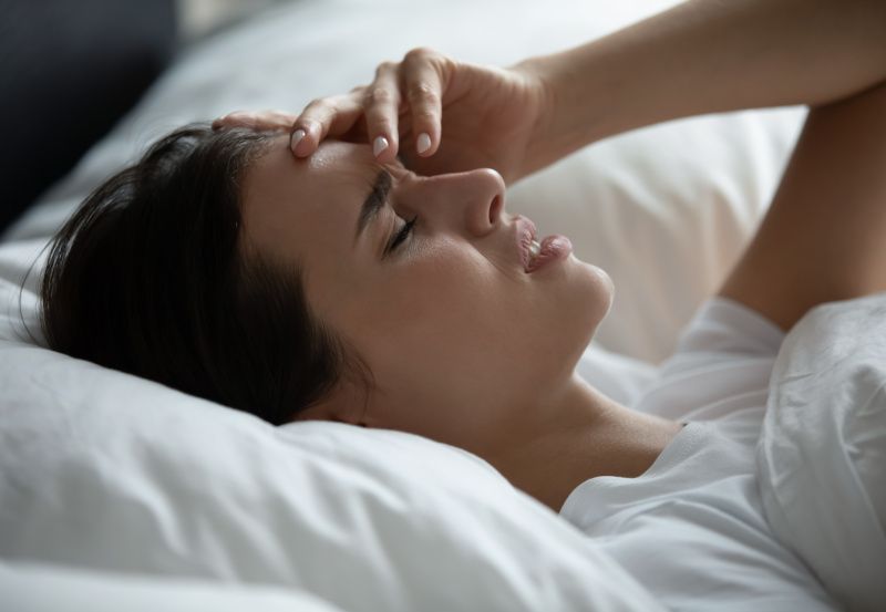 Frau liegt mit Kopfschmerzen im Bett
