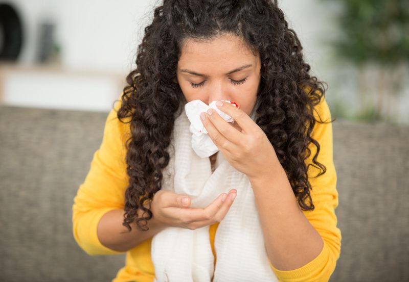 Frau hat Nasenbluten und hält sich Taschentuch vor die Nase