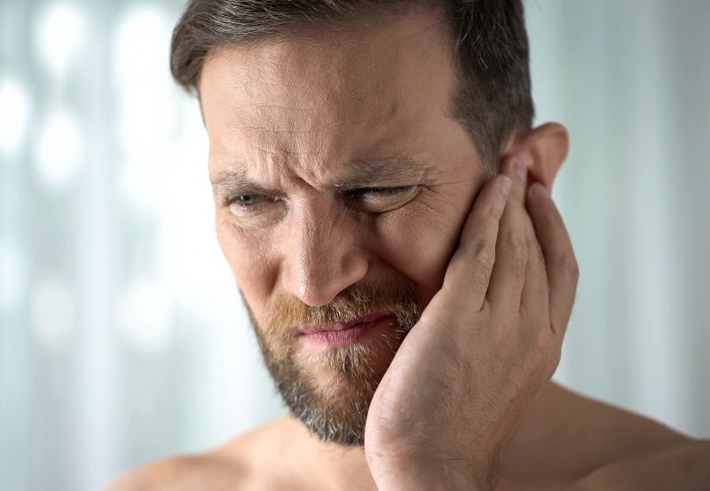 Mann mit Ohrenschmerzen hält sich das Ohr zu