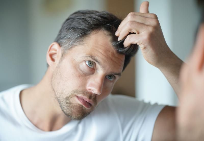 Mann betrachtet seine Haare im Spiegel