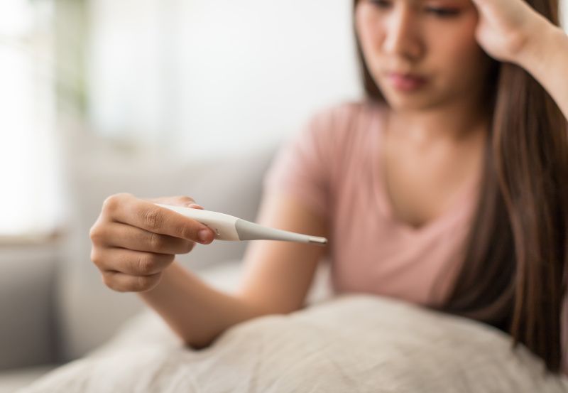 Frau mit Fieberthermometer im Bett