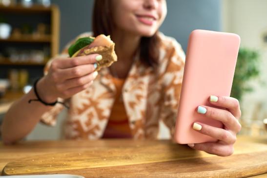 Junges Mädchen schaut ins Smartphone während sie etwas isst