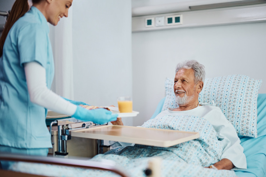 Pflegeassistentin bringt Patient im Krankenbett Essen