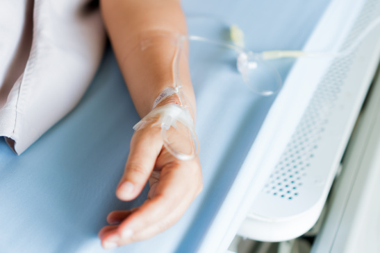 Hand eines Patienten im Krankenhausbett mit Infusion