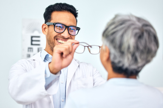Fröhlicher Orthoptiker setzt Frau eine Brille auf