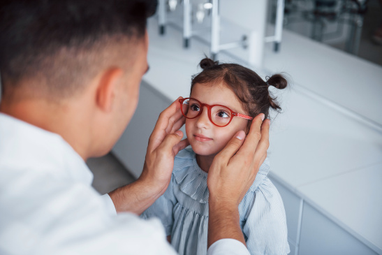 Augenarzt setzt einem Mädchen eine Brille auf