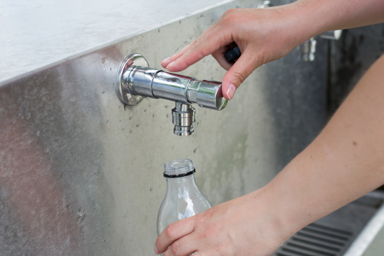 Person füllt Wasserflasche an einem öffentlichen Wasserhahn auf