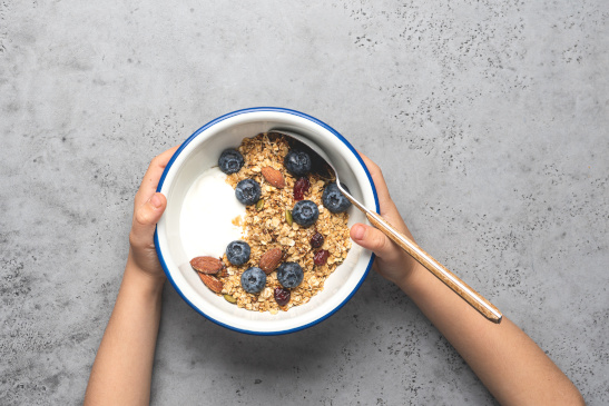 Hände eines Kindes halten Schüssel mit Müsli und Obst