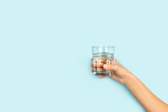 Hand mit Wasserglas vor blauem Hintergrund