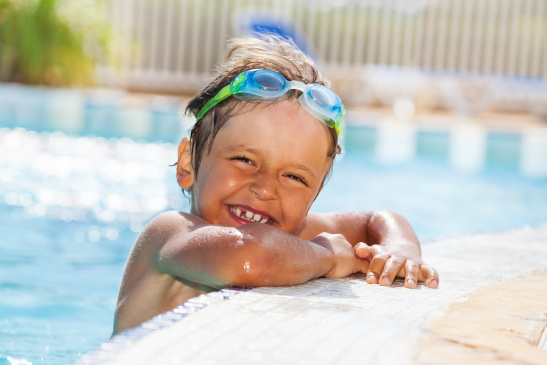 Fröhlicher Bub hält sich am Rand eines Swimmingpools fest