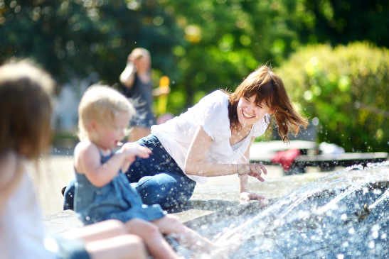 Junge Frau und zwei Kinder kühlen sich bei einem Brunnen in der Stadt ab