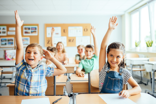 Schulkinder in der Klasse zeigen auf 