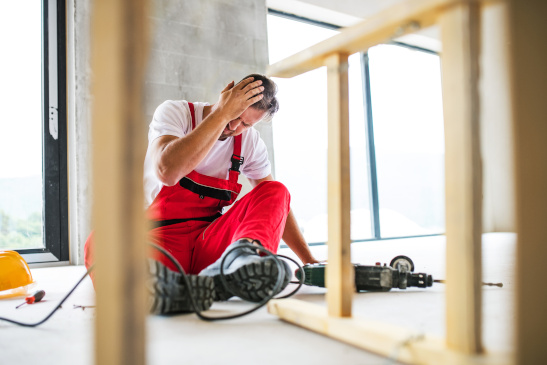 Mann ist auf einer Baustelle von der Leiter gefallen und hat Kopfschmerzen