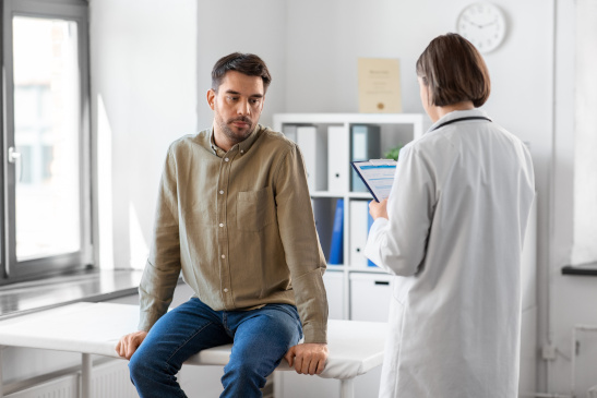 Patient sitzt auf einer Liege und spricht mit einer Ärztin