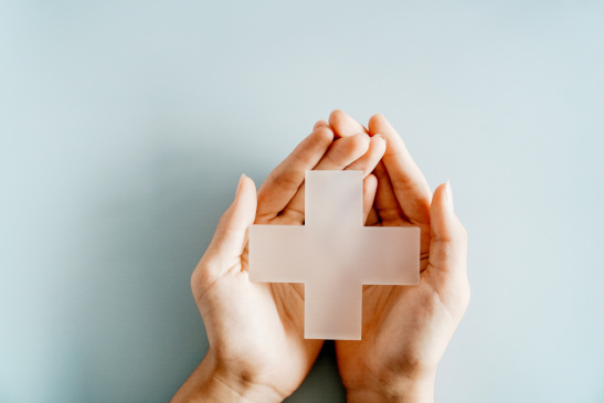 Hände halten weißes Kreuz