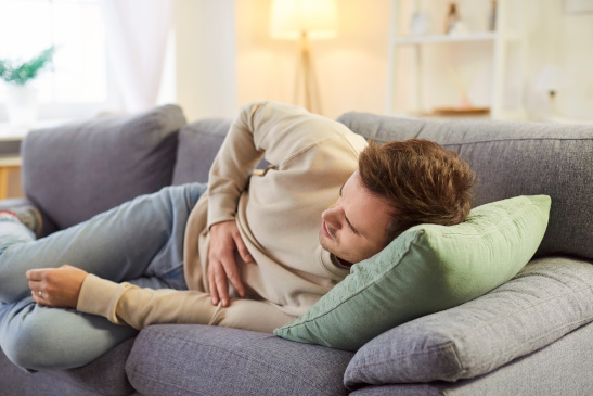 Mann liegt auf der Couch und hat Bauchschmerzen