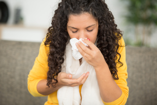 Frau mit Nasenbluten hält sich Taschentuch vor die Nase