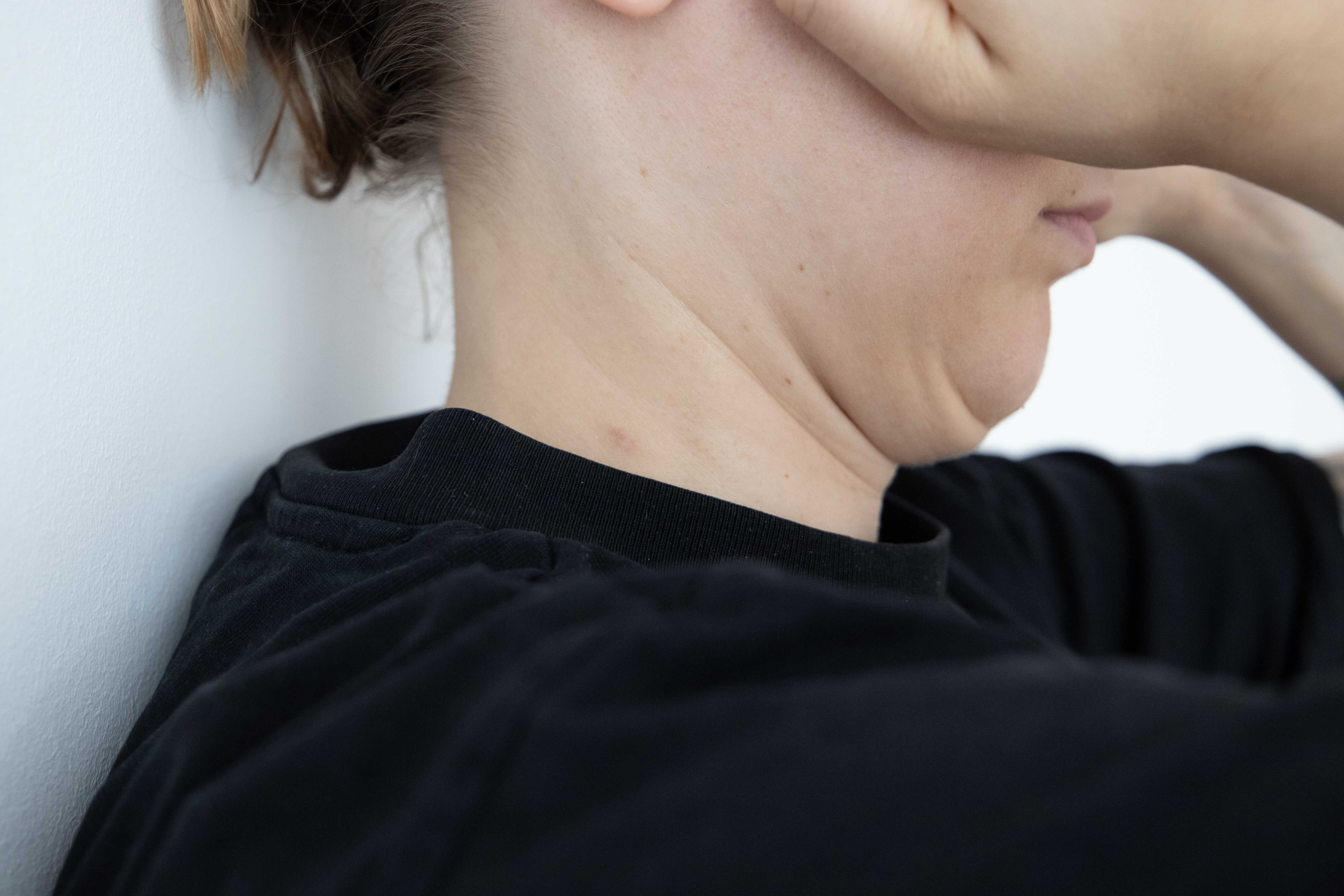 Frau steht mit Rücken an der Wand und zieht Kinn nach hinten