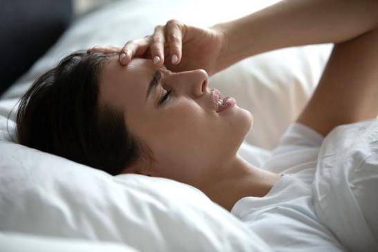 Frau liegt mit starken Kopfschmerzen im Bett