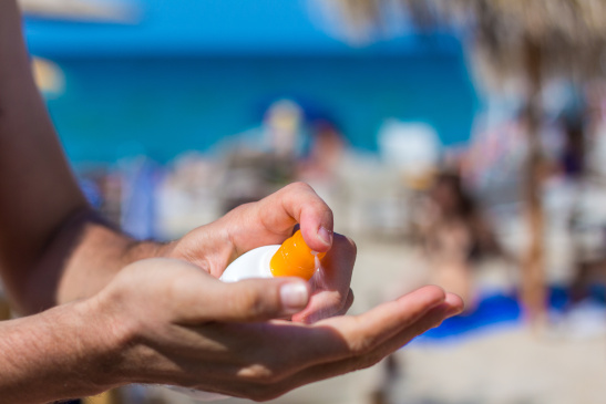 Mann sprüht sich Sonnencreme in die Hand